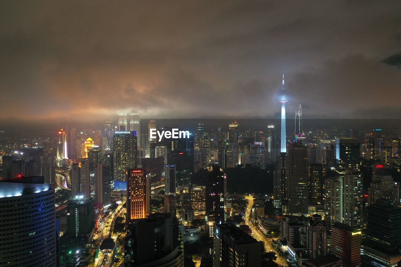 Illuminated modern buildings in city against sky at night