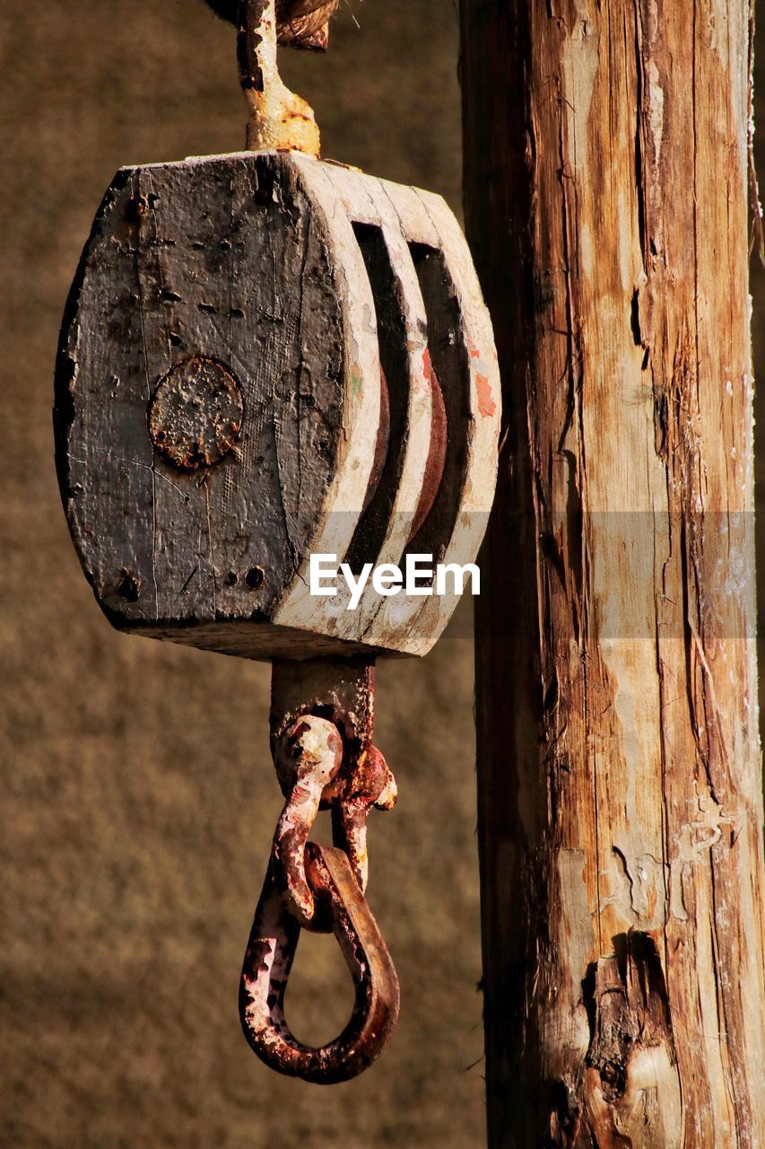 Close-up of rusty pulley hanging from wooden post