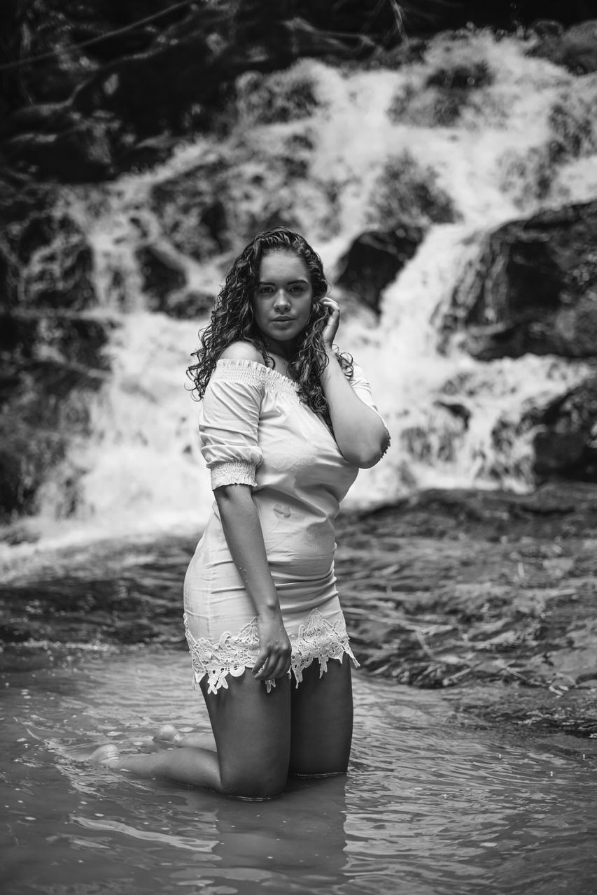 PORTRAIT OF WOMAN STANDING AGAINST WATERFALL