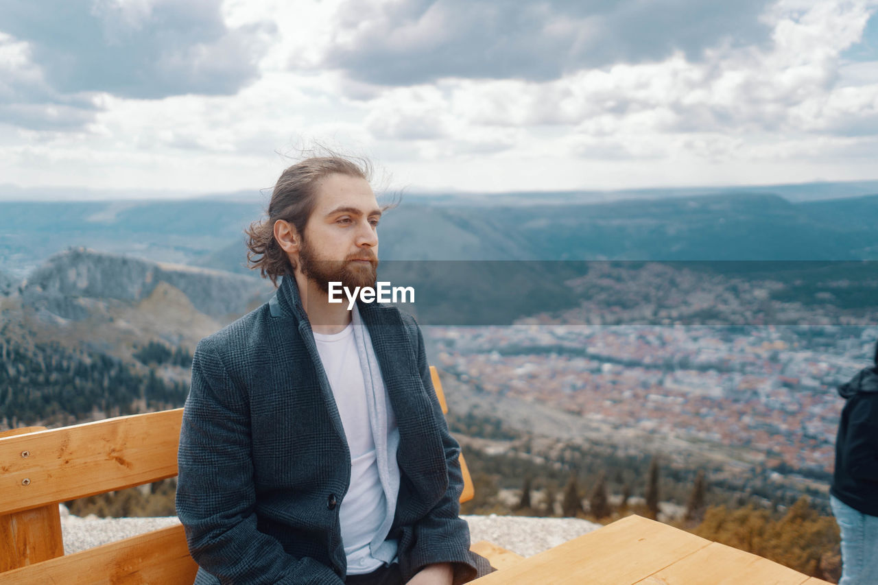 Young man looking at cityscape against sky