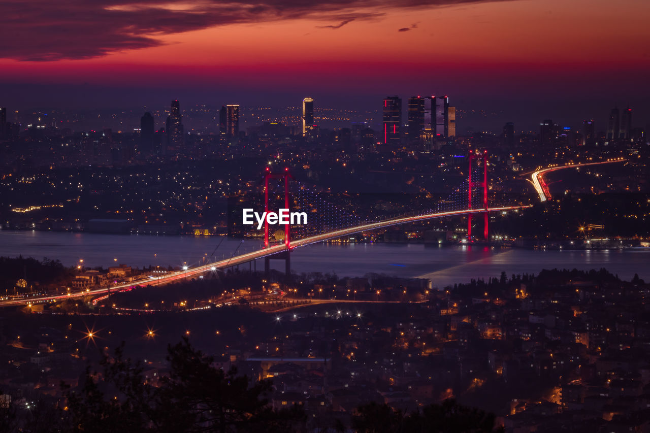 Illuminated city by river against sky at night