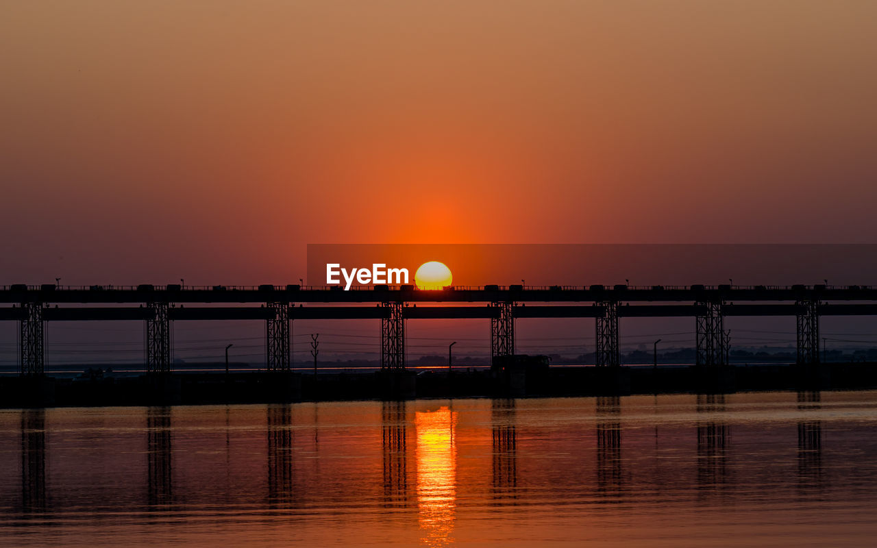 sunset, water, sky, reflection, nature, beauty in nature, dawn, sea, tranquility, orange color, scenics - nature, silhouette, sun, architecture, afterglow, tranquil scene, no people, bridge, built structure, horizon, idyllic, evening, outdoors, travel destinations, transportation, waterfront, sunlight, dramatic sky, pier, travel