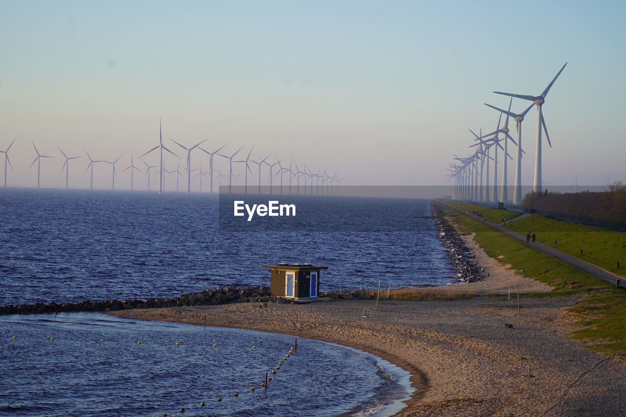 Scenic view of wind turbines at sea against sky during sunset