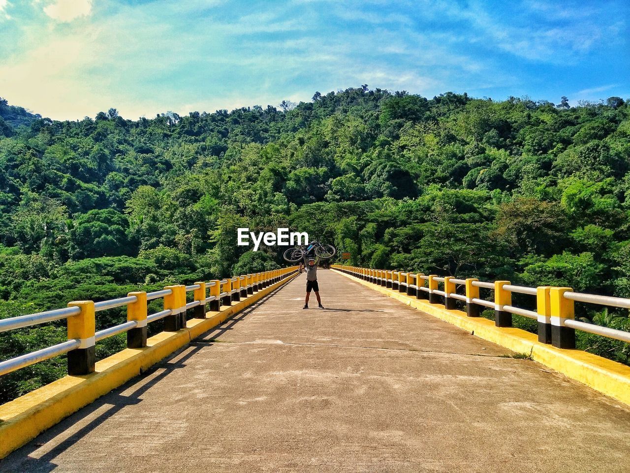 Full length of man holding bicycle while standing on bridge against mountains