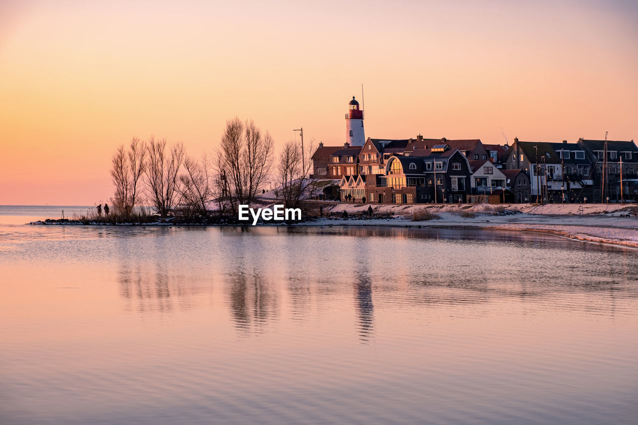 REFLECTION OF BUILDING IN LAKE AGAINST SKY DURING SUNSET