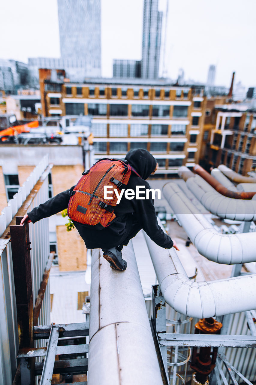 Side view of man with backpack crouching on pipe