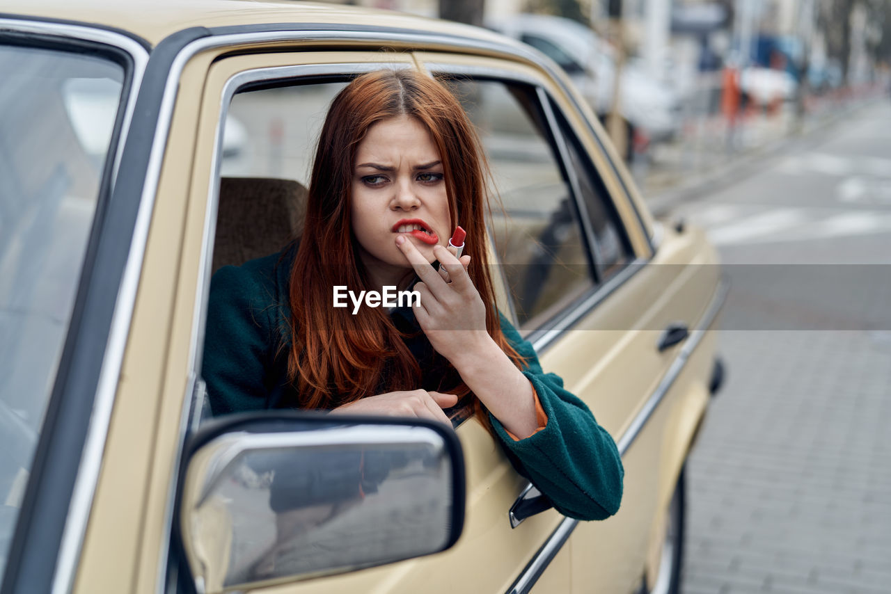 young woman using mobile phone while sitting in car in city