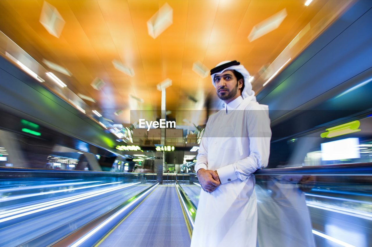 Man standing amidst blurred motion of light trails at railroad station