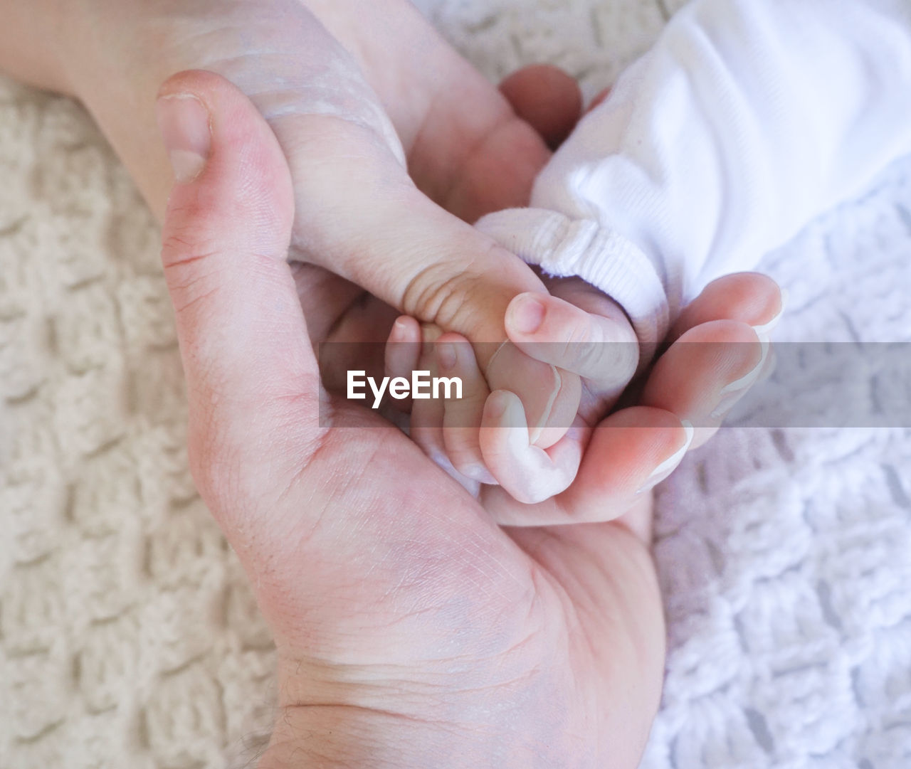 Cropped image of parents holding baby hand on bed