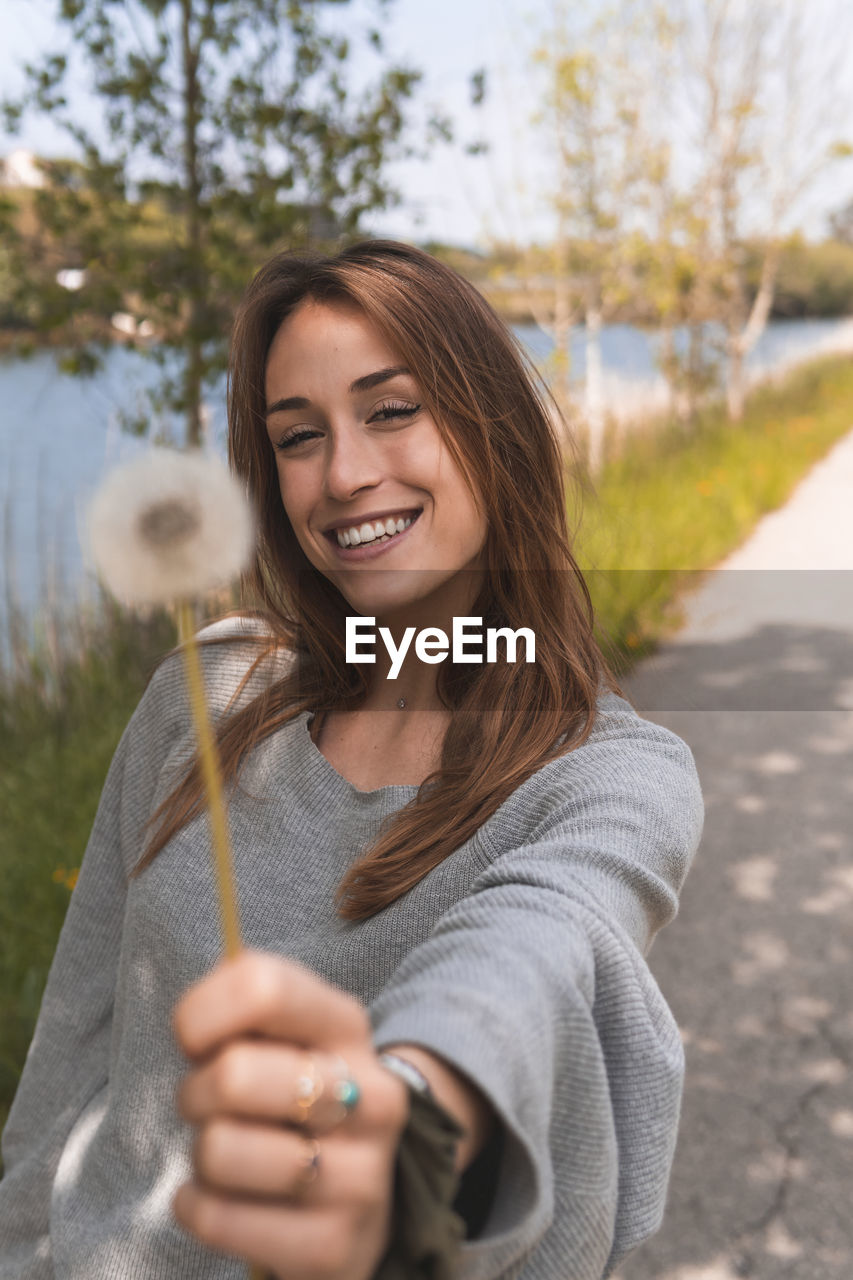 Smiling woman showing blowball in nature