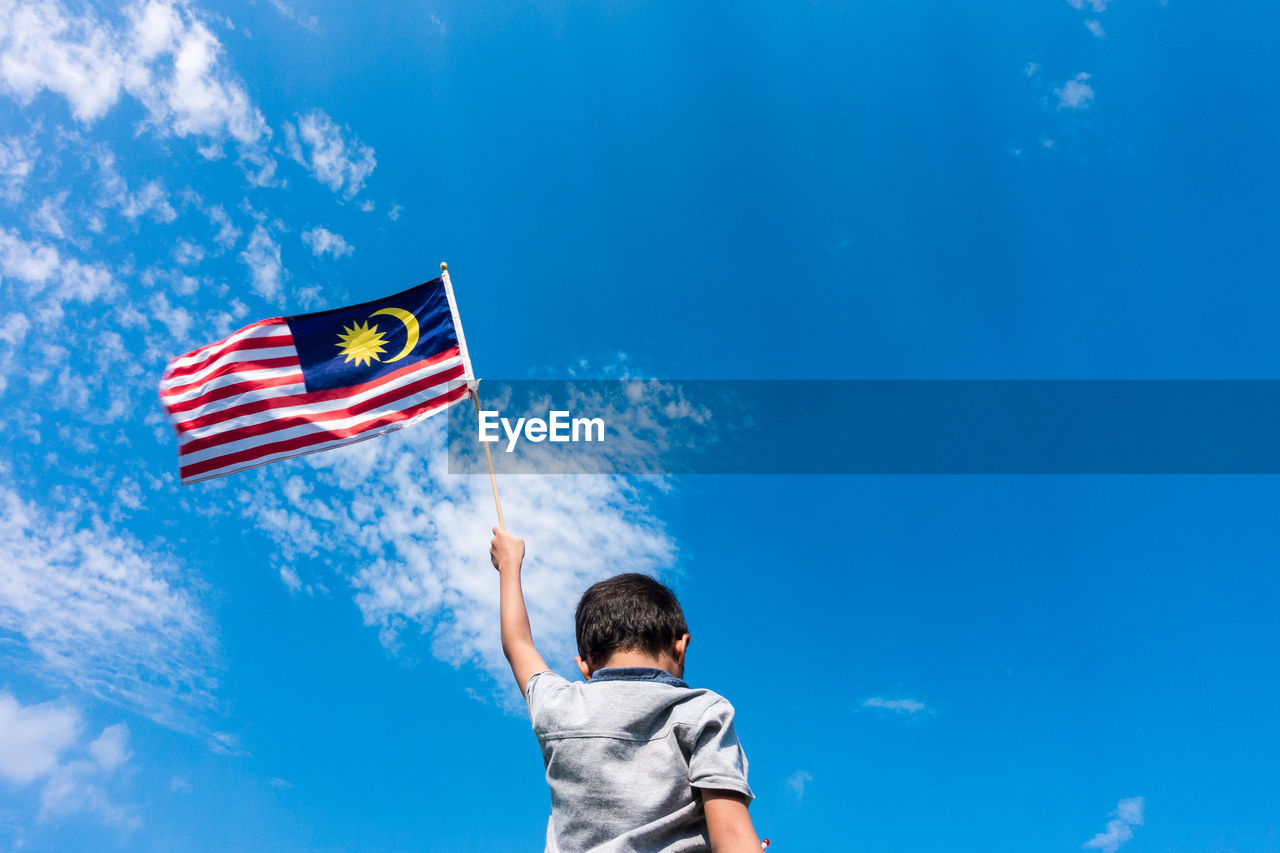 LOW ANGLE VIEW OF BOY HOLDING KITE AGAINST BLUE SKY