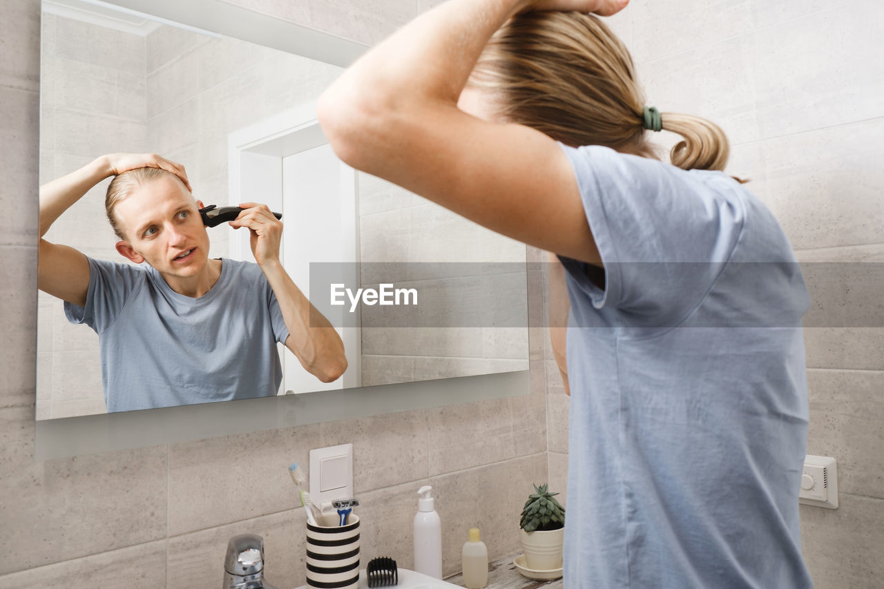 Personal hygiene, caucasian man cutting his own hair in the bathroom with wireless electric shaver