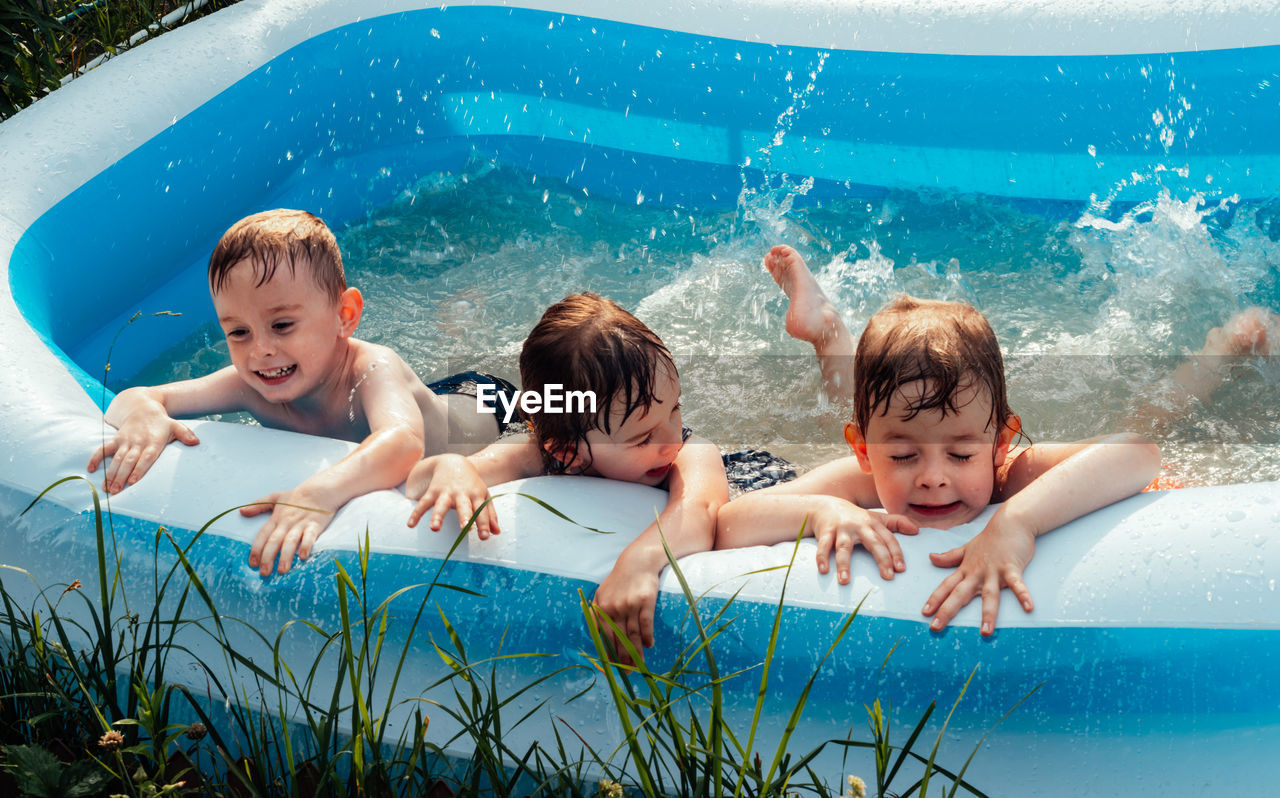 Cheerful happy children lie in the pool and splash with their feet. friends spend summer leisure 