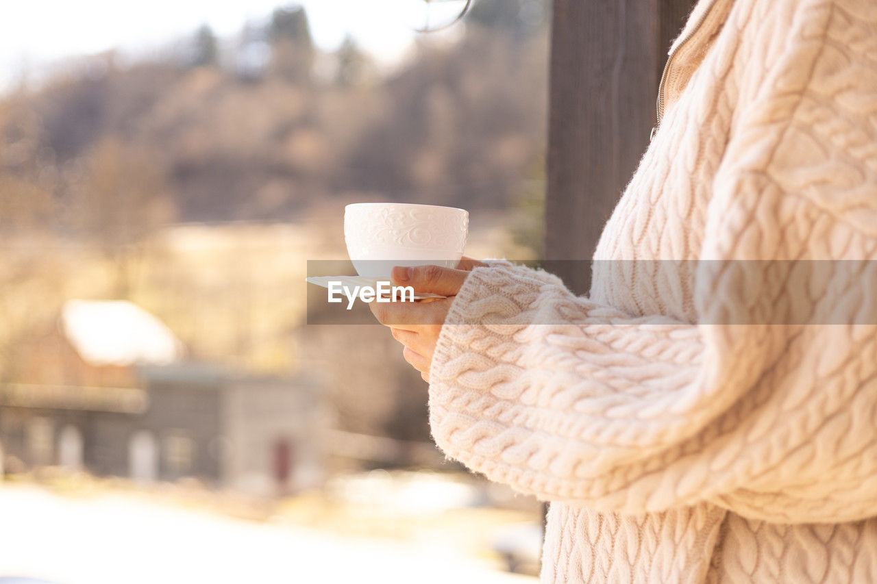 Female hands in a sweater hold a cup of coffee