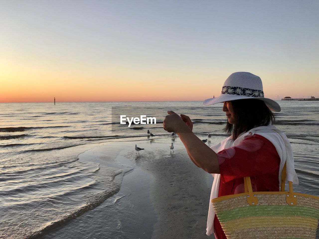 Side view of woman at beach against sky during sunset