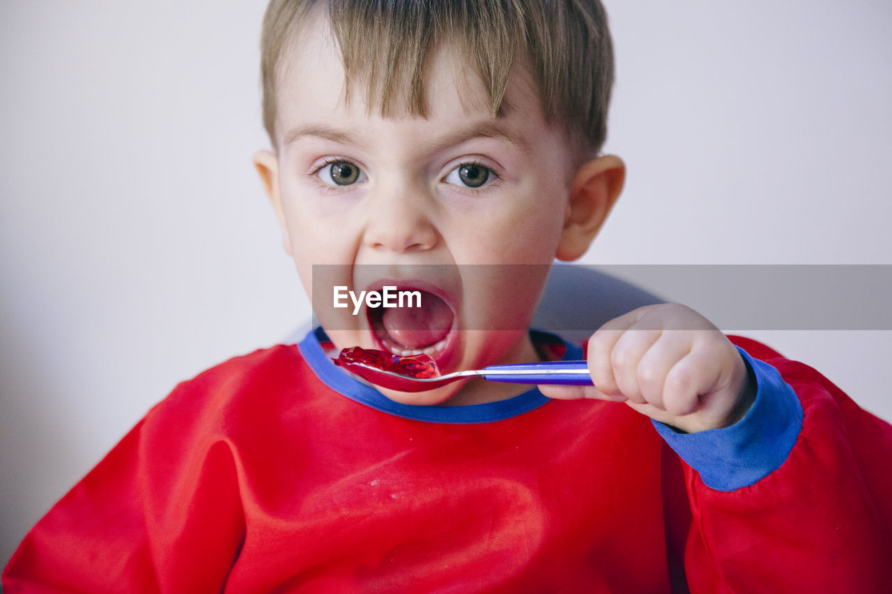 Close-up portrait of cute baby boy eating food against wall