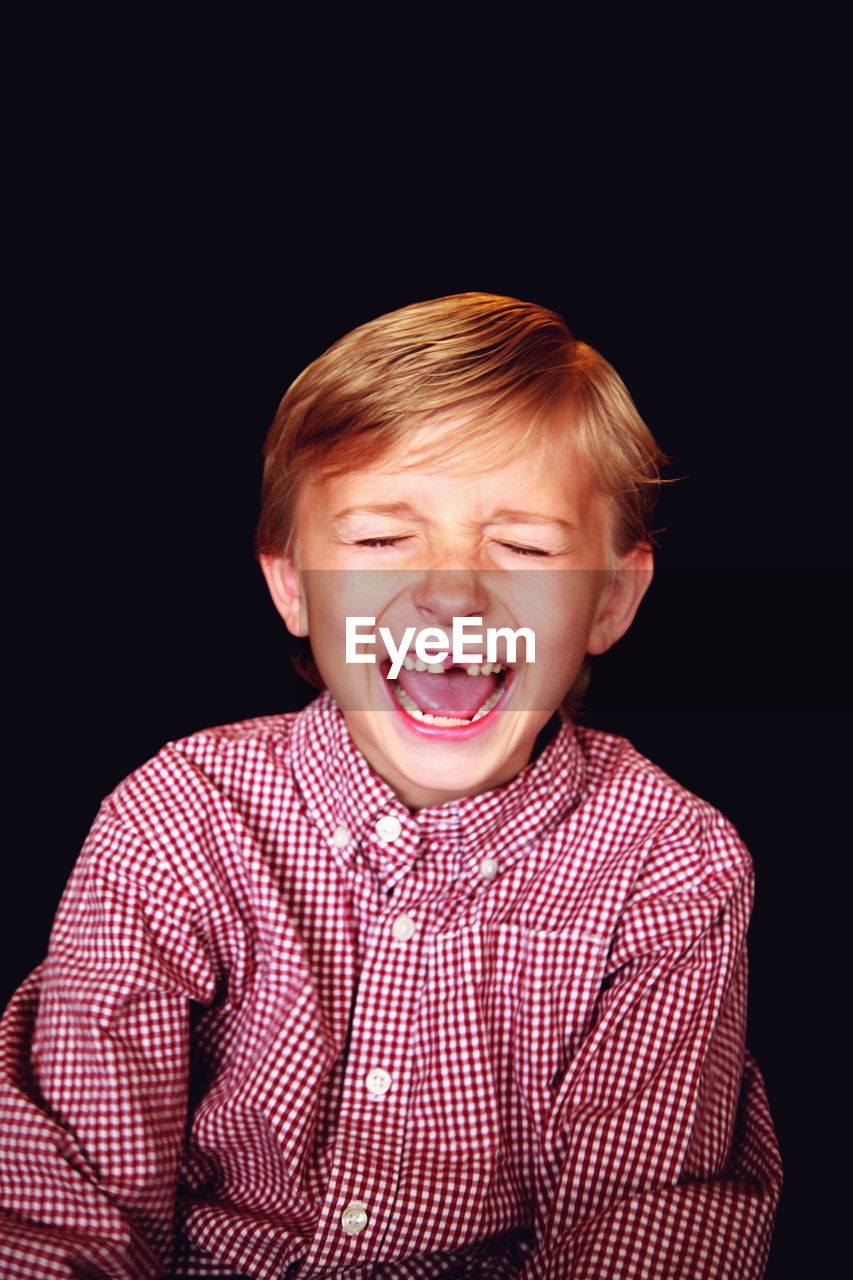 Boy laughing with eyes closed against black background