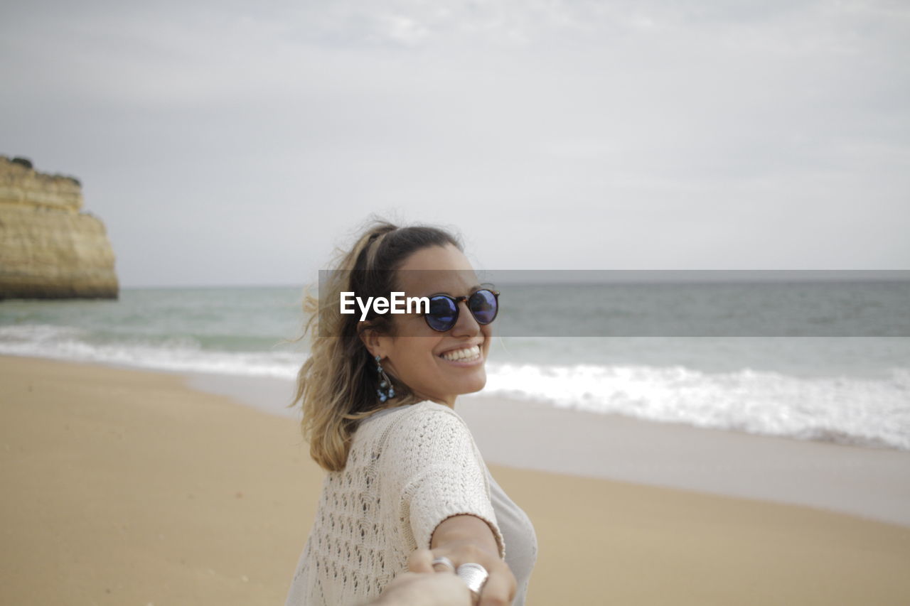 Cropped hand holding smiling woman at beach