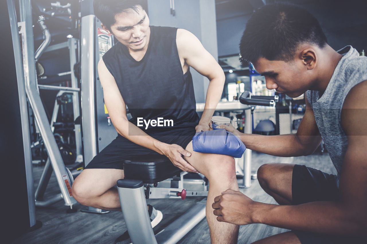 Trainer looking at injured man leg in gym