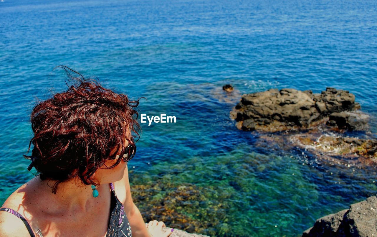 Woman wearing sunglasses sitting by sea