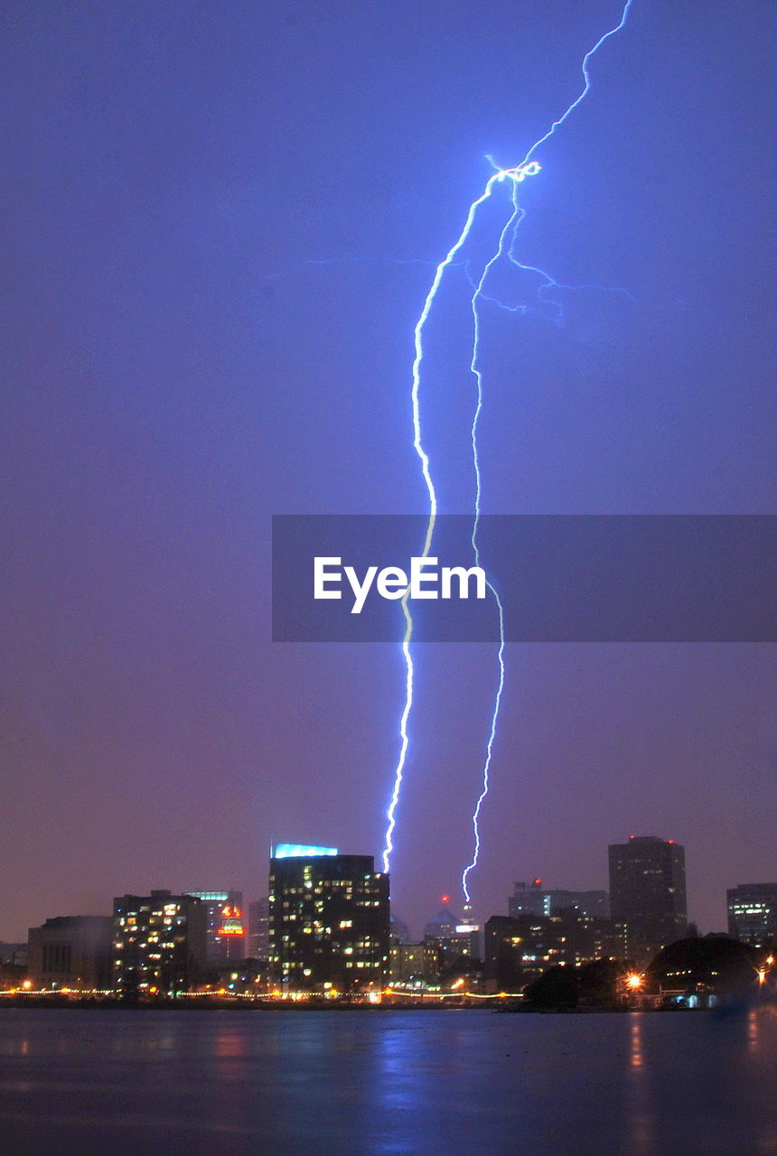 Low angle view of lightning over illuminated buildings against sky in city at dusk