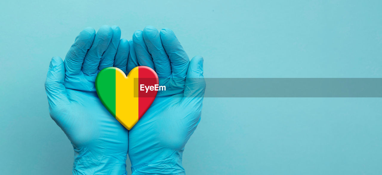 CLOSE-UP OF PERSON HOLDING HEART SHAPE OVER BLUE BACKGROUND