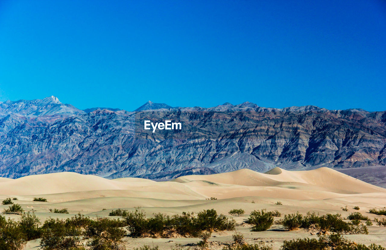 Scenic view of sand dune next to mountain against clear sky