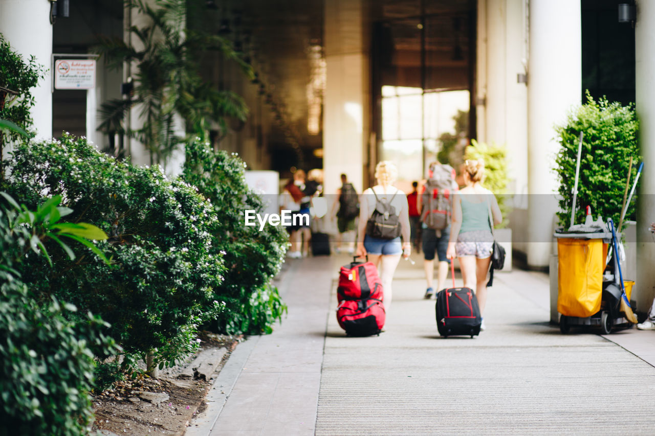 PEOPLE WALKING ON STREET AMIDST PLANTS