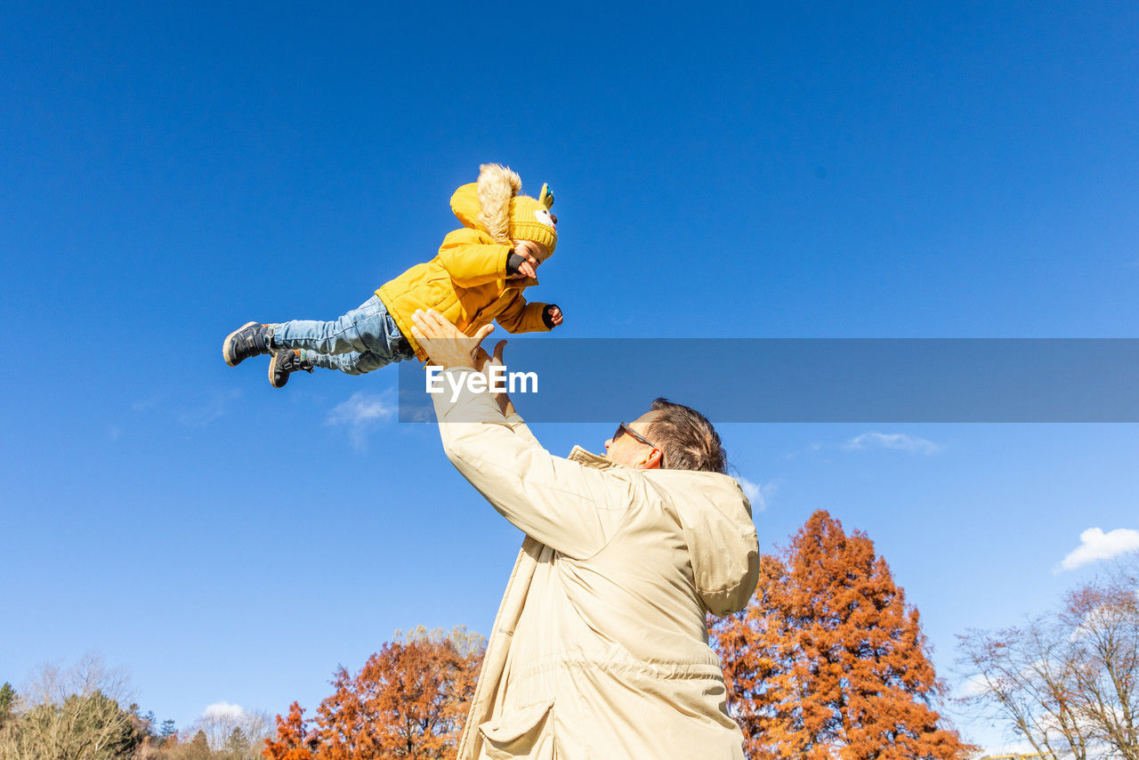 low angle view of woman with arms raised standing against blue sky