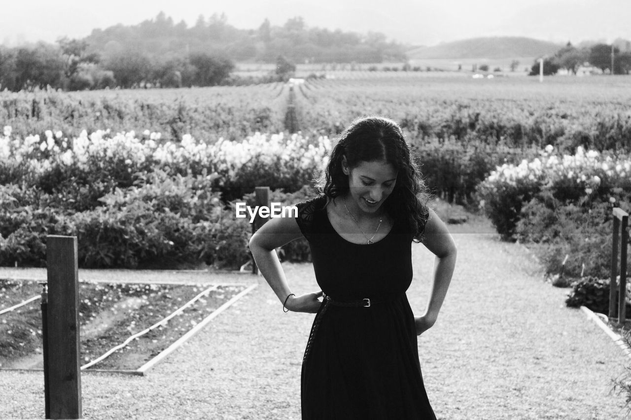 SMILING YOUNG WOMAN STANDING IN FIELD