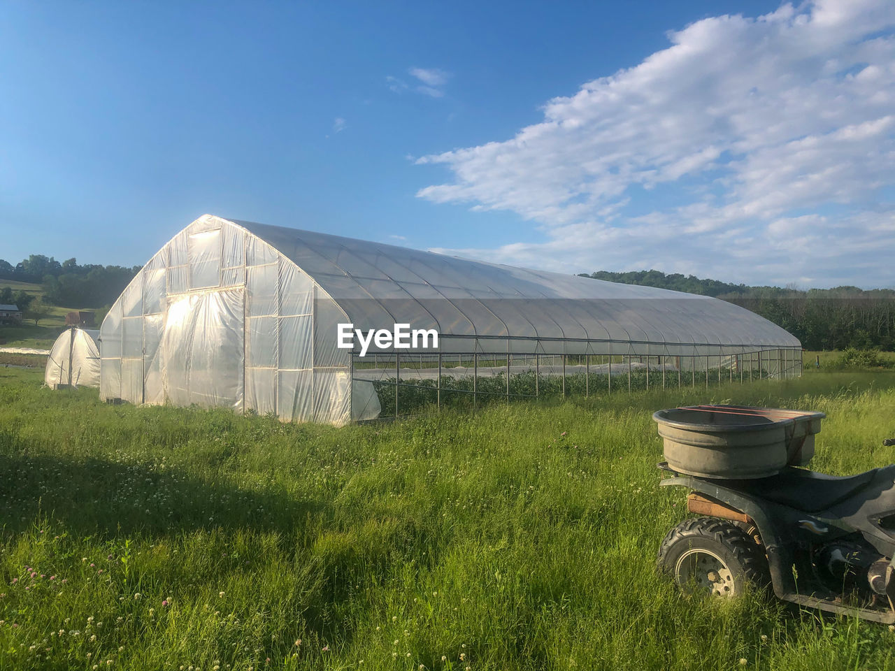 Scenic view of agricultural field against sky with greenhouse and off road vehicle