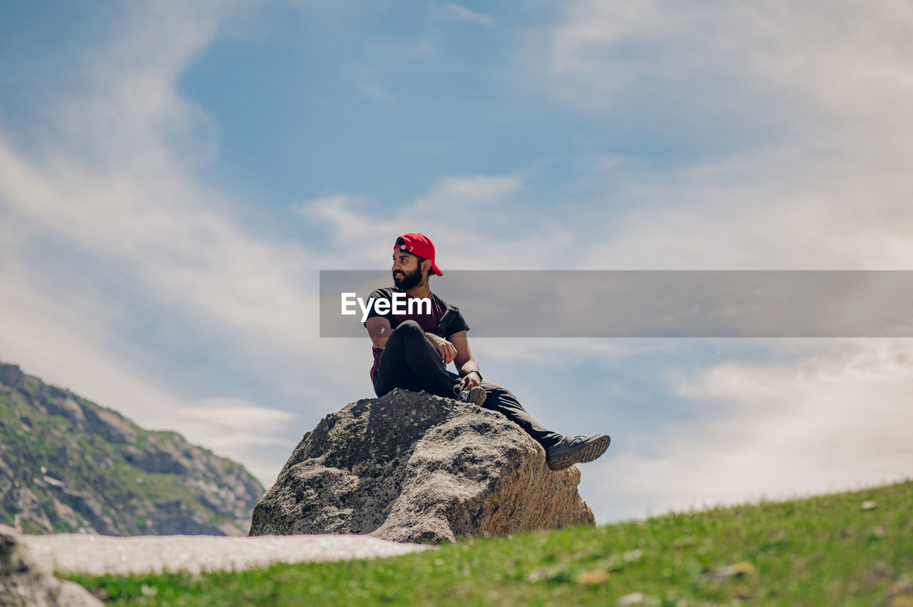 Low angle view of man sitting on rock against sky