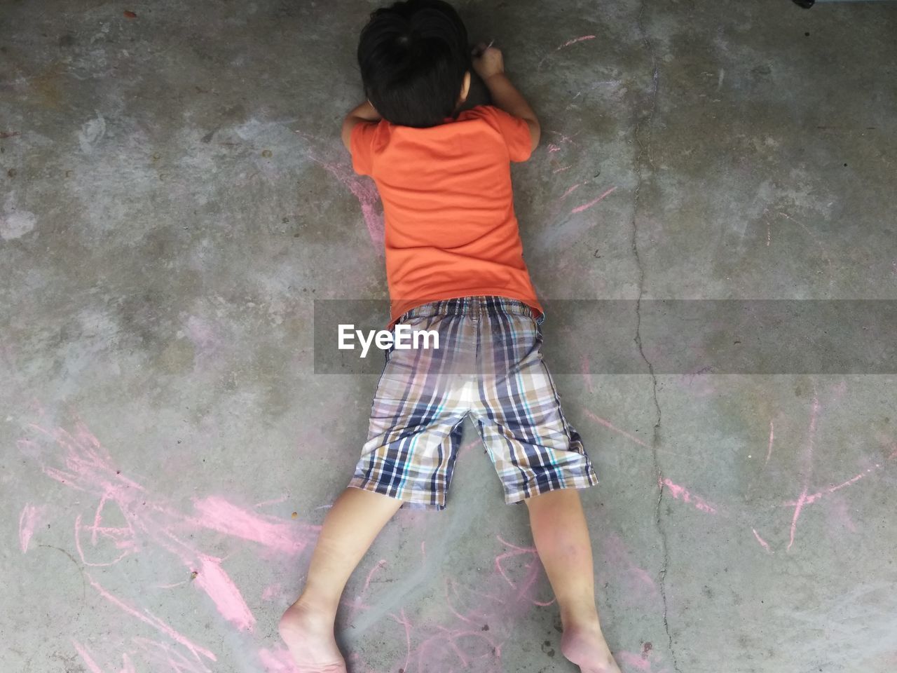 High angle view of boy drawing with chalk while lying on footpath