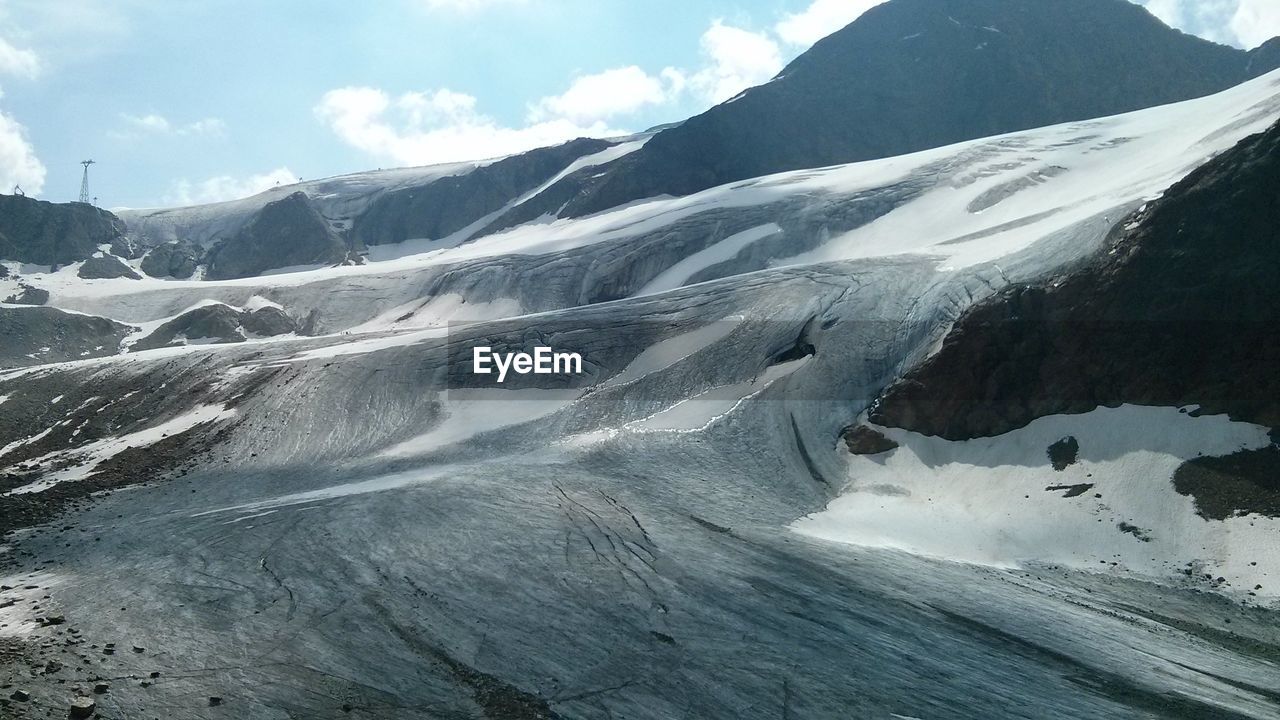 Scenic view of snow covered mountains against cloudy sky