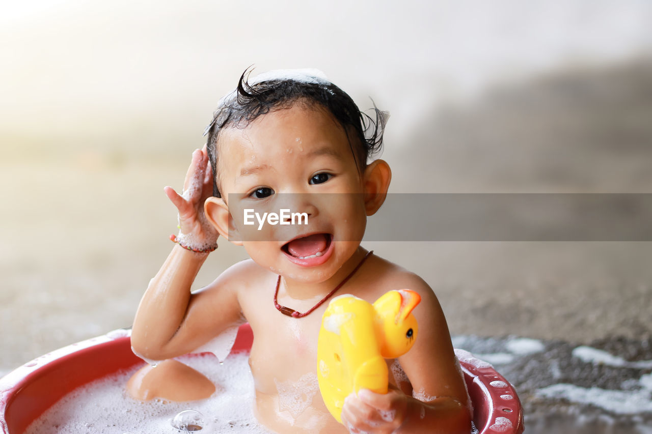 Cheerful shirtless baby girl sitting in bathtub