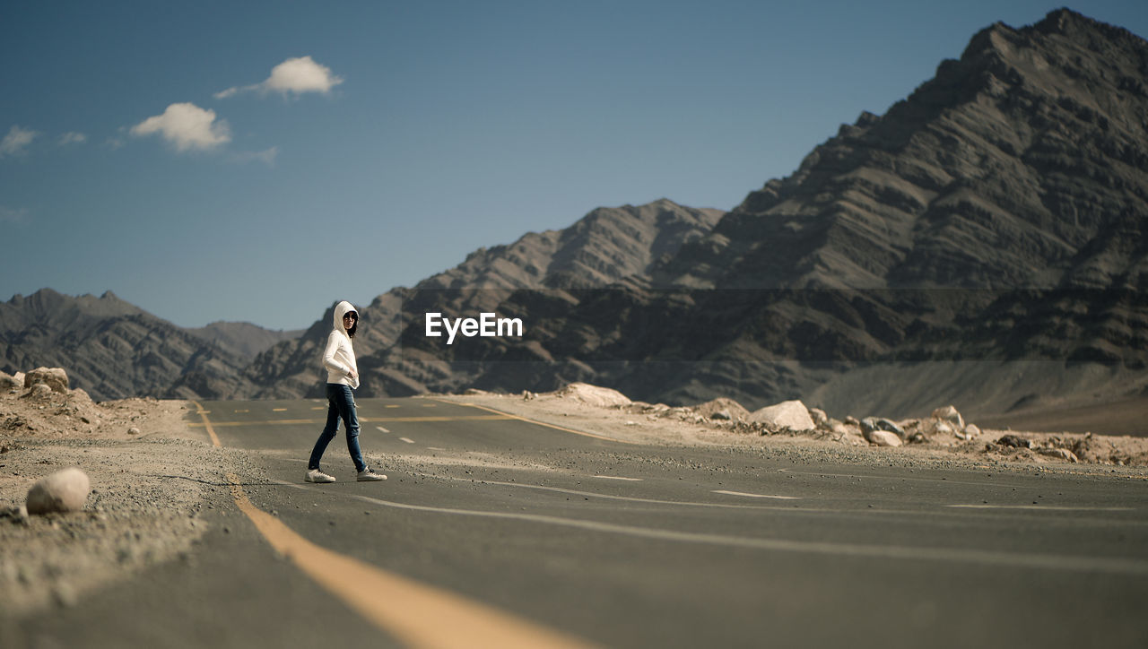 Woman walking on road by mountains against sky