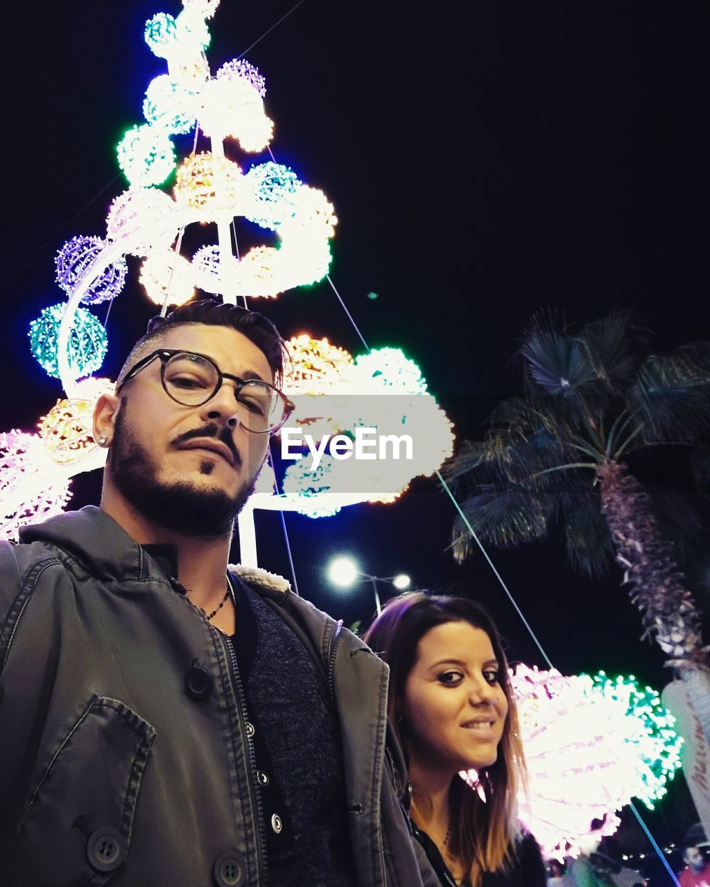 Portrait of young couple against illuminated christmas tree
