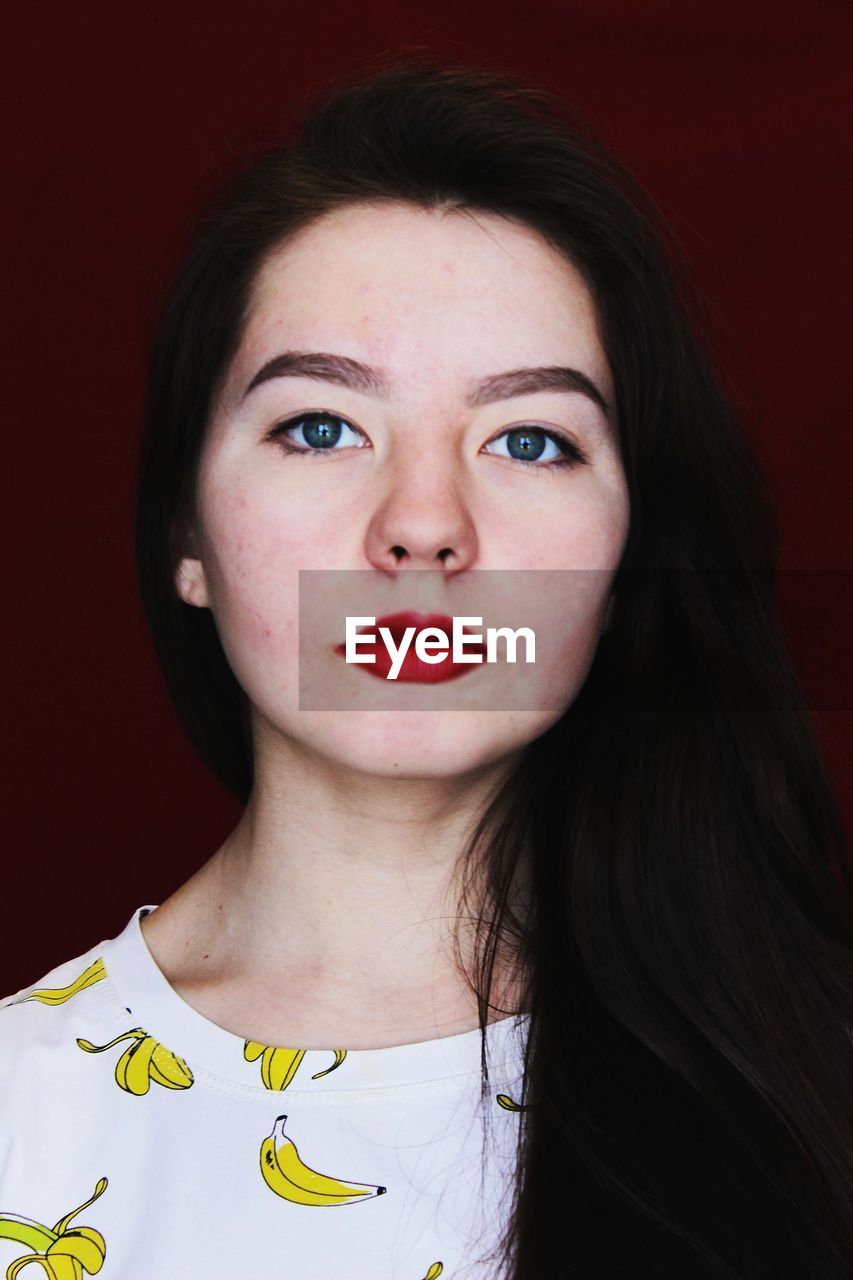 Portrait of beautiful young woman against maroon wall