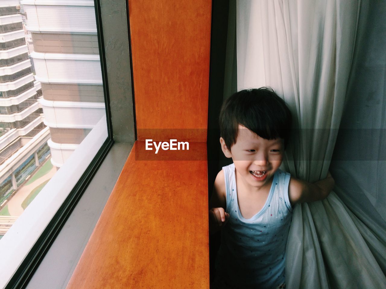 Cute playful boy standing by window at home