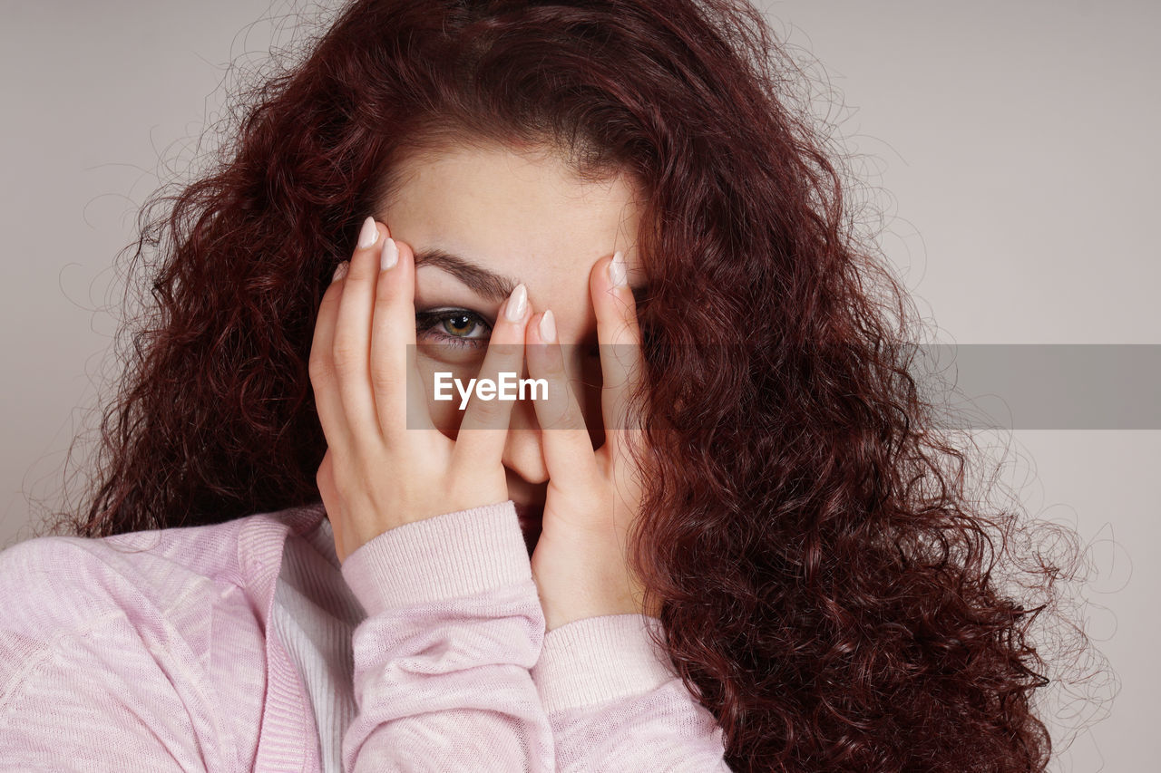 Portrait of young woman covering face against beige background