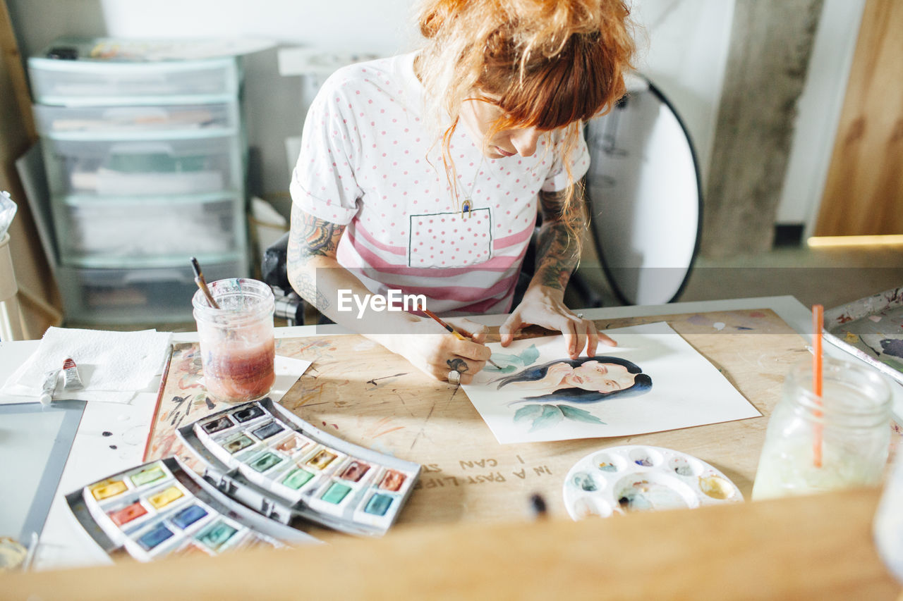 High angle view of artist painting while standing at table in studio