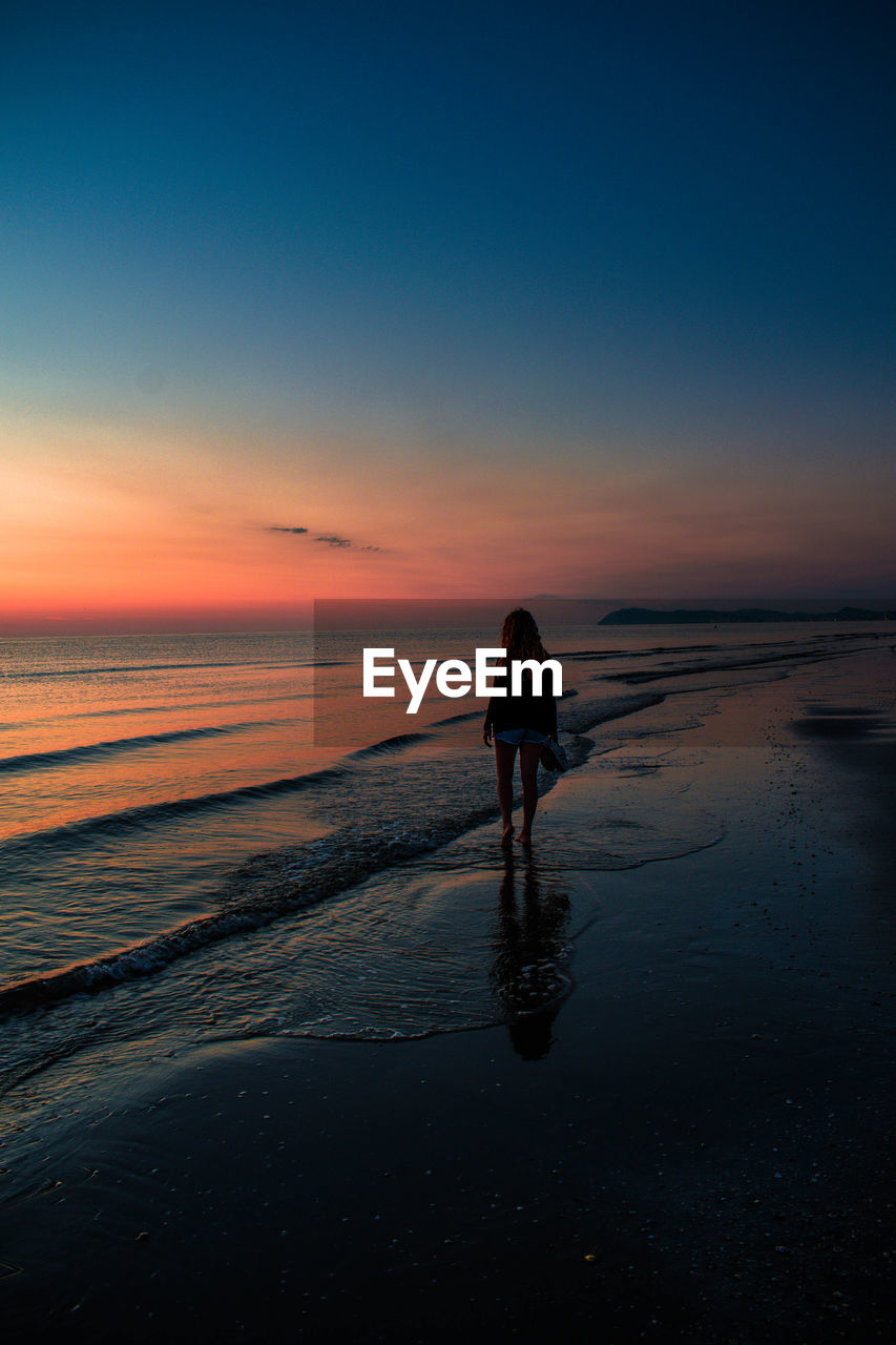 Rear view of silhouette man walking on beach during sunset