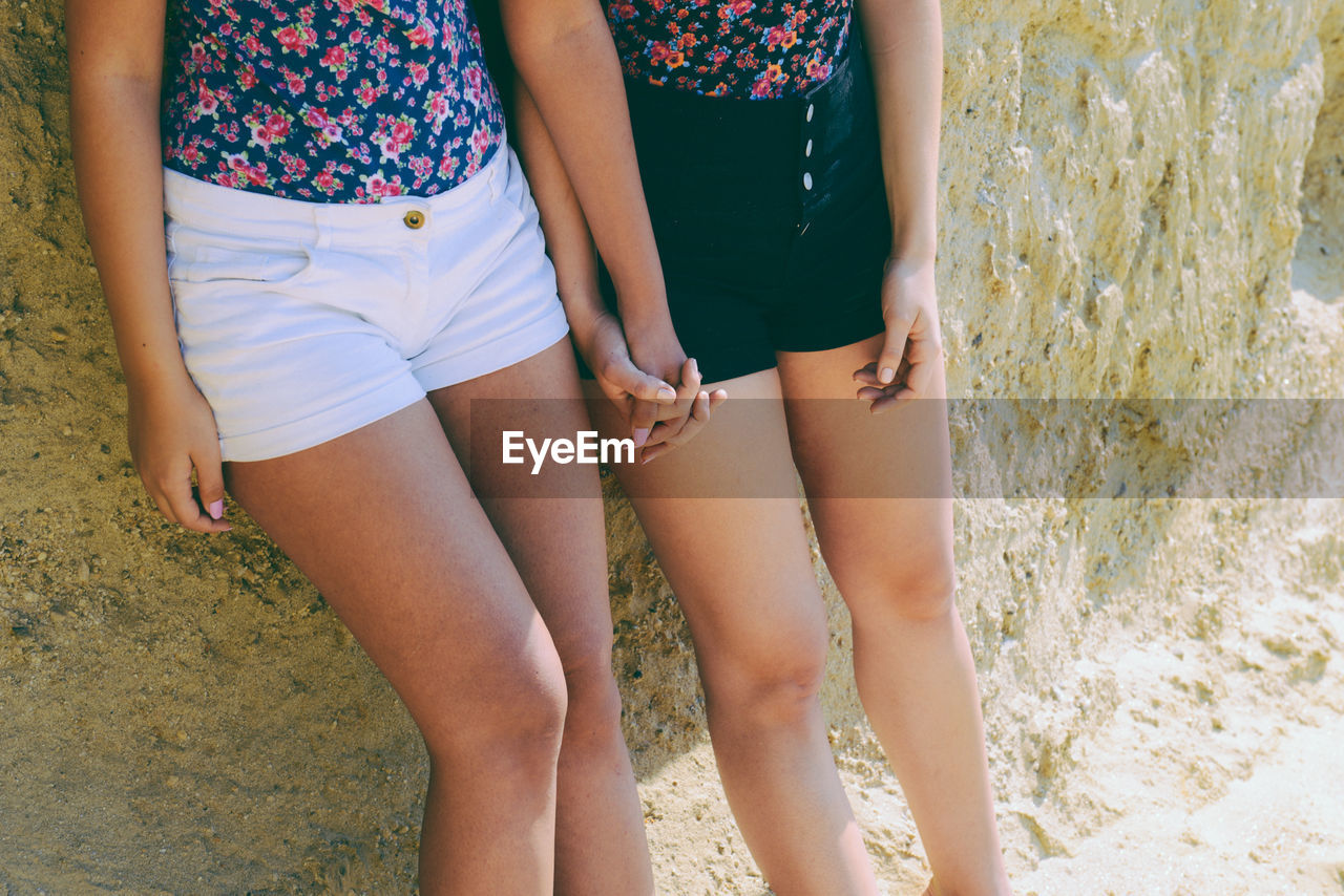 Midsection of friends holding hands while leaning on wall