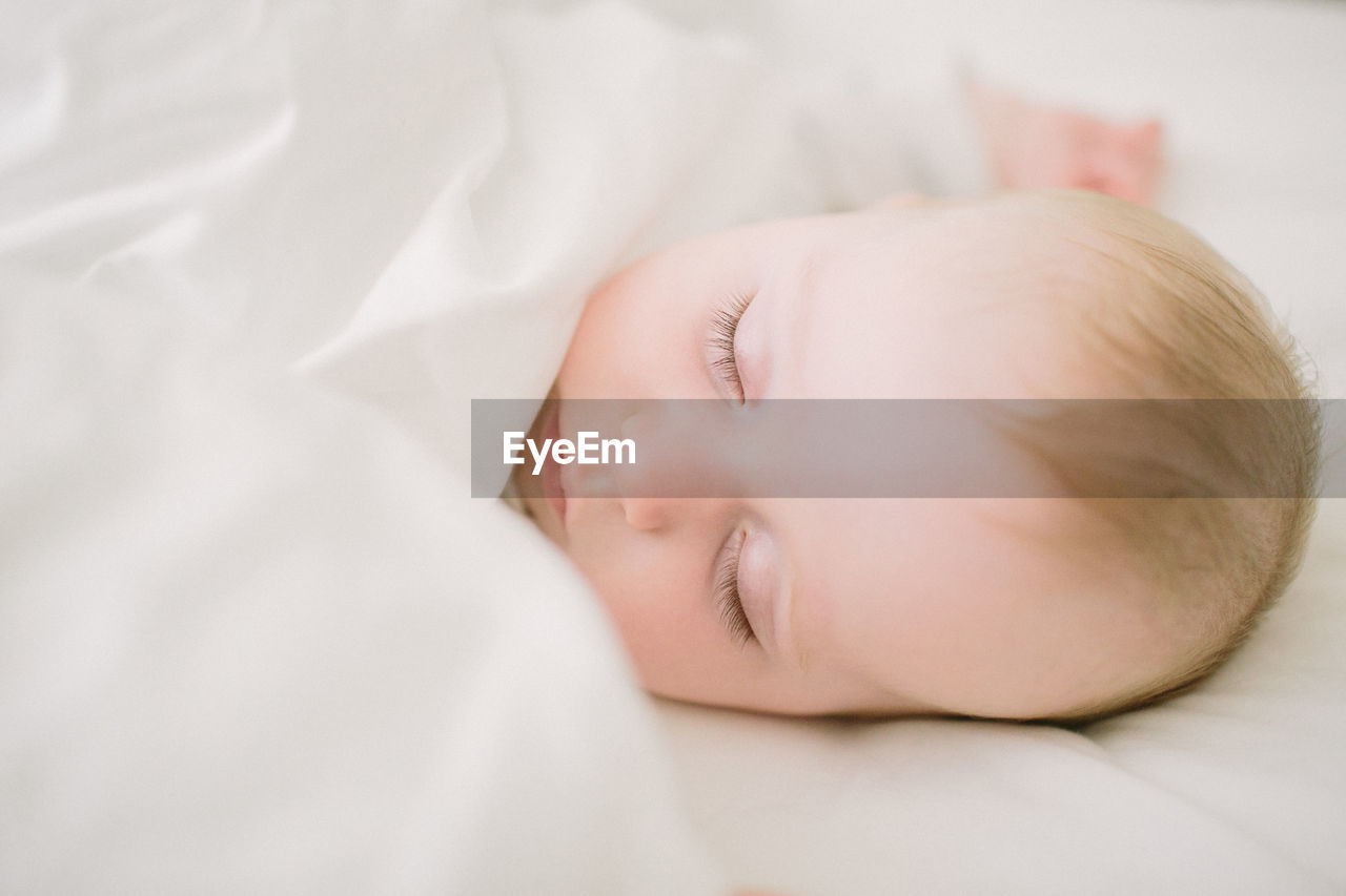 Peaceful and ethereal sleeping baby surrounded in white blanket