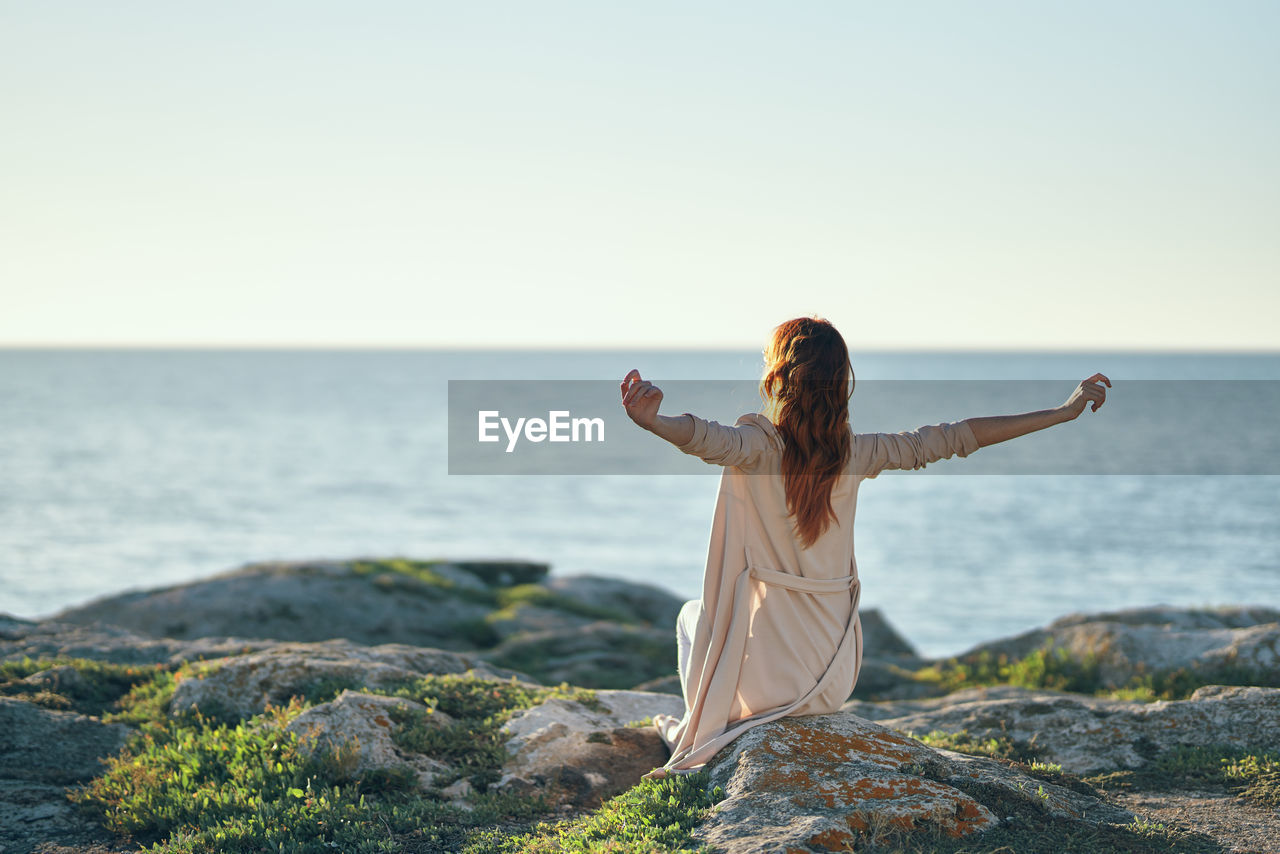 Rear view of woman on rock against clear sky