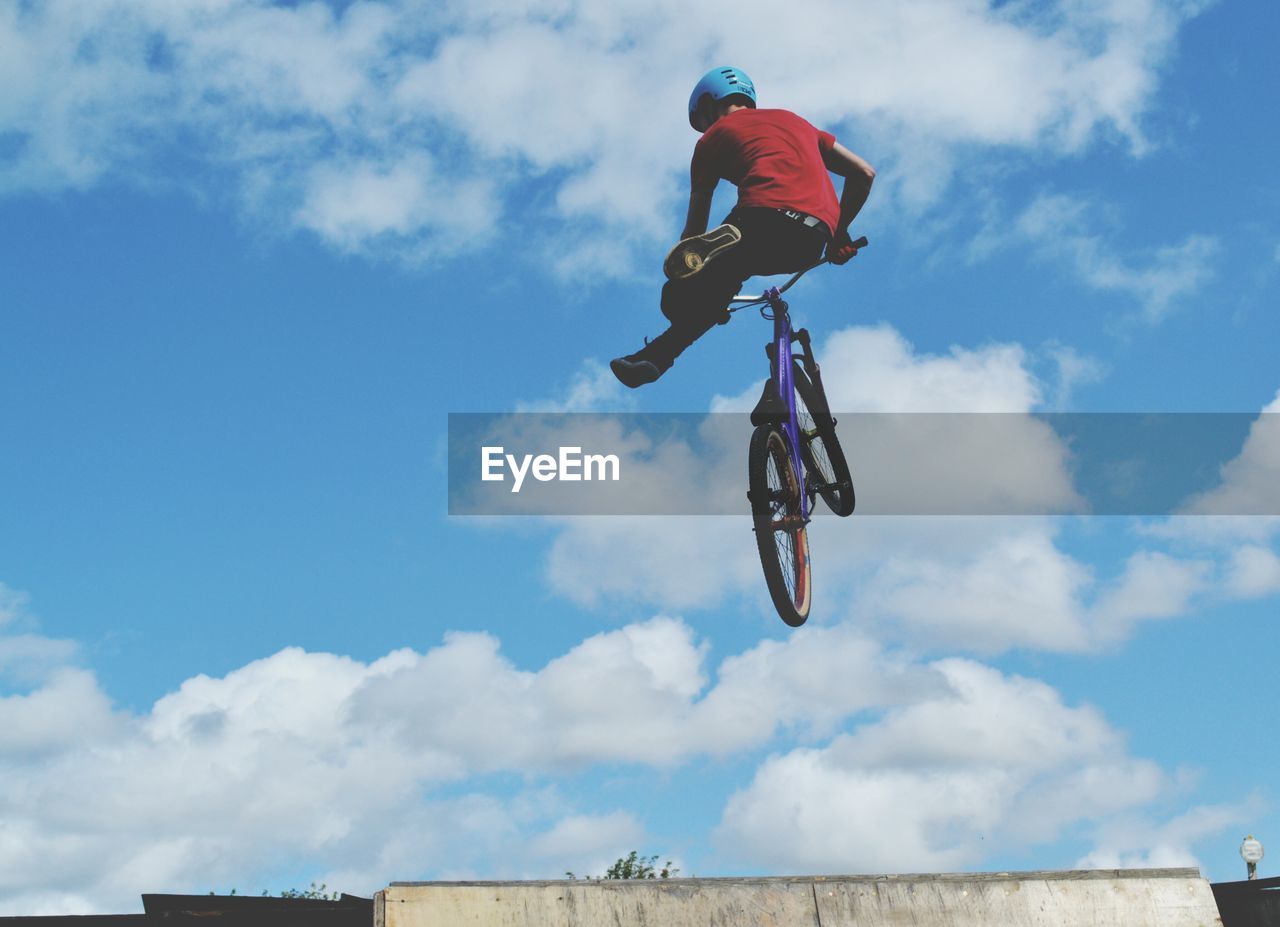 Low angle view of man jumping with bicycle against sky