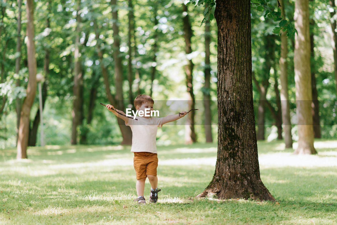 Little caucasian boy playing outdoors in the park with a stick from a tree