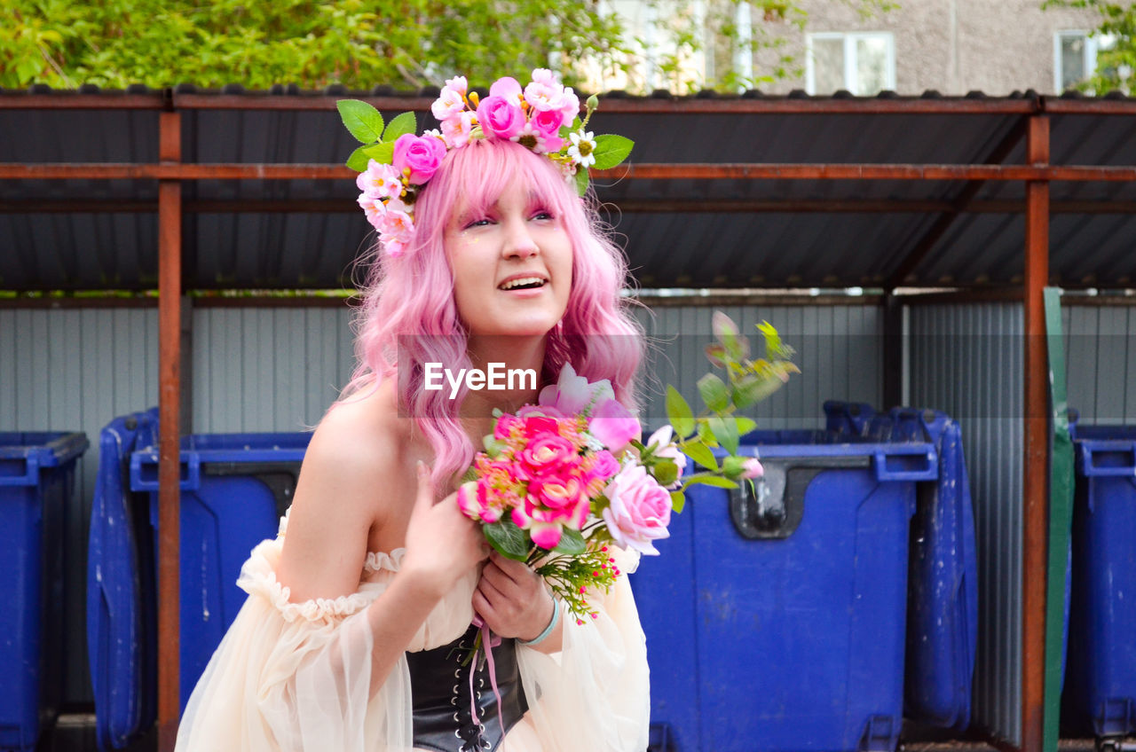Portrait of smiling young woman holding bouquet against the backdrop of trash