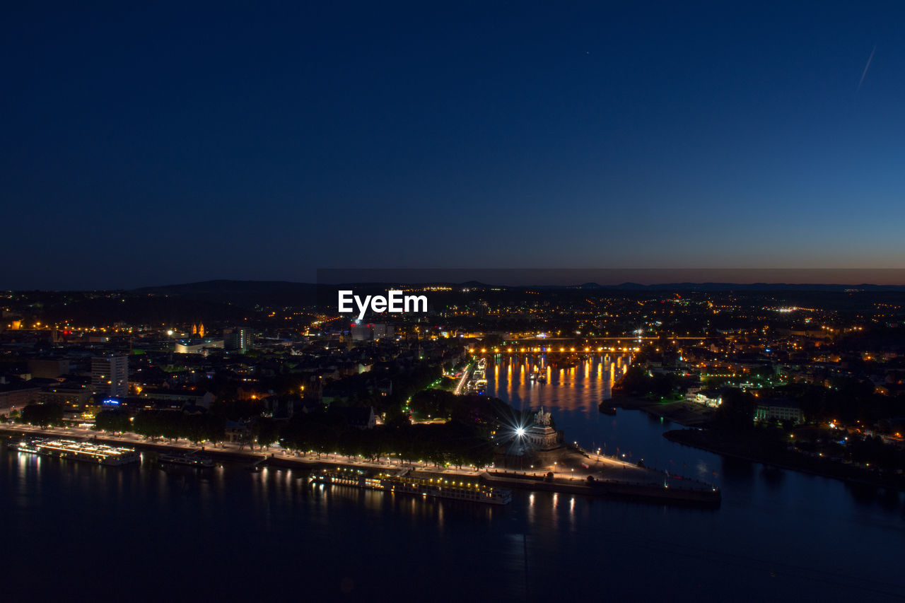 Illuminated cityscape against clear blue sky at night