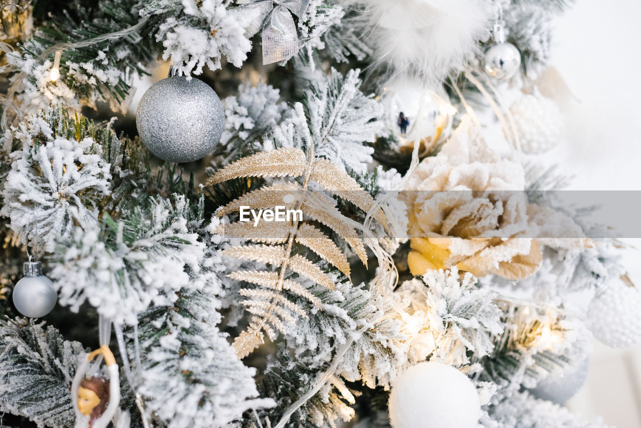 Christmas decorations in the form of a rose, a fern leaf and balls hang on a silver christmas tree